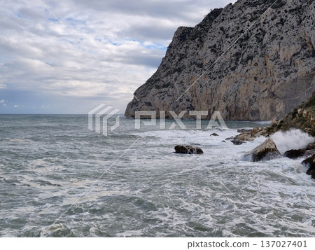 Jagged limestone face with foaming waves beneath stormy sky showcasing natural geological processes 137027401