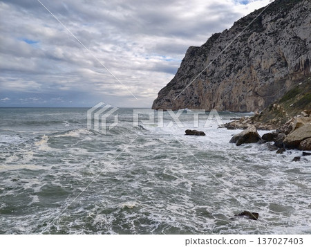 Churning waves crash onto shoreline, Vigorous ocean with frothy breakers beneath turbulent skies Churning waves crash onto shoreline, Vigorous ocean with frothy breakers beneath turbulent skies 137027403