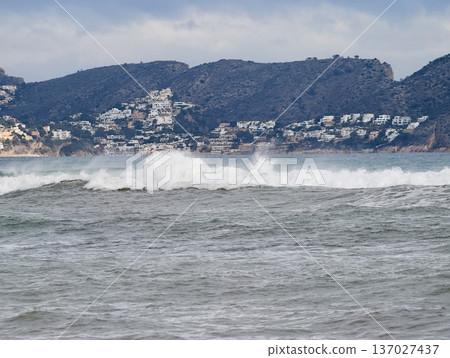 Wild sea crashes on coastal terrain, Aggressive waves strike rugged shoreline near resort buildings 137027437