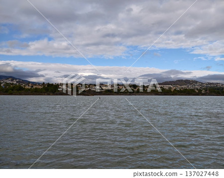 Peaceful water view with mountain and sky, Calm waters and distant town over serene sheltered bay 137027448