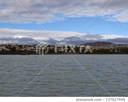 Vast water scene, Expansive waters beneath dramatic clouds framing rugged ridge and nearby small town Vast water scene, Expansive waters beneath dramatic clouds framing rugged ridge and nearby small town 137027449