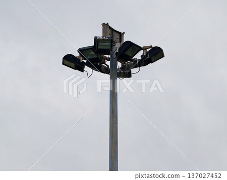Vertical metallic pole decorated with industrial lamps against overcast city sky background 137027452