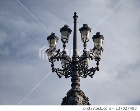 Decorative streetlight under cloudy sky, Ornate cast iron lamppost with multiple lanterns overhead 137027498