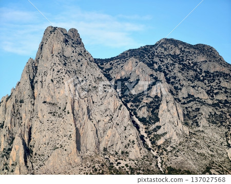 Dark narrow path winding through towering stone peaks under dramatic late daylight conditions Dark narrow path winding through towering stone peaks under dramatic late daylight conditions 137027568