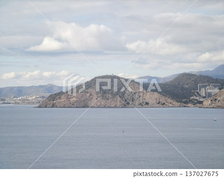Peaceful solitary island set against tranquil sea with distant mountain ranges and gentle clouds Peaceful solitary island set against tranquil sea with distant mountain ranges and gentle clouds 137027675