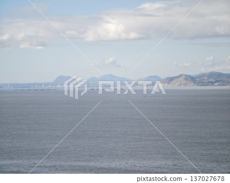 Serene coastal scenery, Gentle clouds cast soft shadows over lofty peaks surrounding calm and silent sea Serene coastal scenery, Gentle clouds cast soft shadows over lofty peaks surrounding calm and silent sea 137027678