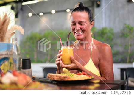 Happy Mature Woman Enjoying Healthy Breakfast Outdoors in Coffee Shop Happy Mature Woman Enjoying Healthy Breakfast Outdoors in Coffee Shop 137027736