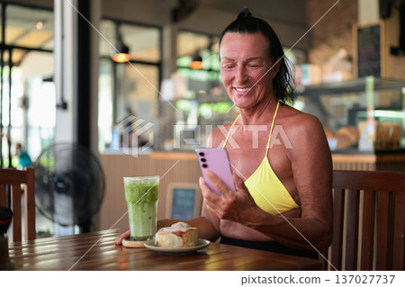 Mature Woman in Bikini Using Smartphone at Cafe with Iced Matcha Latte and Dessert Mature Woman in Bikini Using Smartphone at Cafe with Iced Matcha Latte and Dessert 137027737