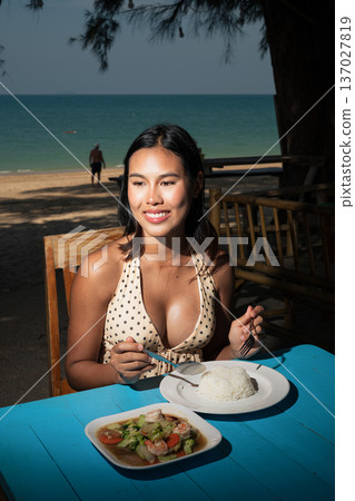 Happy young woman eating rice and shrimp dish while seated at outdoor seaside restaurant Happy young woman eating rice and shrimp dish while seated at outdoor seaside restaurant 137027819