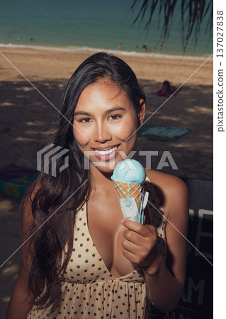 Close-up portrait of smiling woman holding melting ice cream on sunny beach Close-up portrait of smiling woman holding melting ice cream on sunny beach 137027838