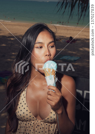 Close-up portrait of smiling woman holding melting ice cream on sunny beach 137027839