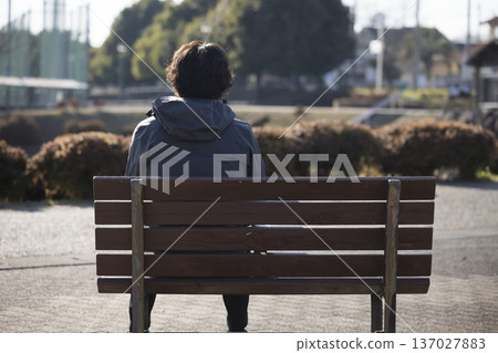 Back view of a middle-aged man sitting alone on a park bench Back view of a middle-aged man sitting alone on a park bench 137027883