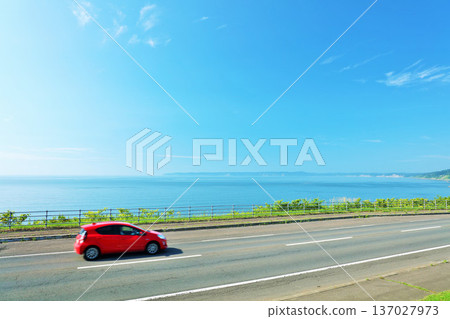 Hokkaido, a red car running on a road along the sea against a blue sky Hokkaido, a red car running on a road along the sea against a blue sky 137027973