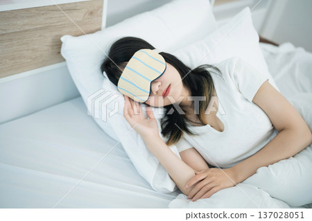 Young woman sleeping peacefully with eye mask in bright bedroom, relaxing atmosphere, cozy bedding and calm environment, ideal for rest and rejuvenation Young woman sleeping peacefully with eye mask in bright bedroom, relaxing atmosphere, cozy bedding and calm environment, ideal for rest and rejuvenation 137028051