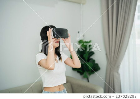 Young Woman Enjoying Virtual Reality Experience with Headset in Modern Living Room with Indoor Plant and Natural Light 137028292