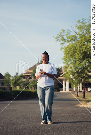 Smiling Mature Scandinavian Tourist Woman Walking Outdoors on Summer Holiday Texting With Phone Smiling Mature Scandinavian Tourist Woman Walking Outdoors on Summer Holiday Texting With Phone 137028826