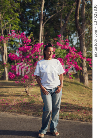 Smiling Mature Woman Standing in Tropical Garden with Pink Flowers 137028830