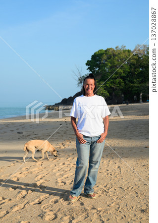 Mature woman standing on tropical beach wearing 90s style normcore fashion jeans and white t-shirt Mature woman standing on tropical beach wearing 90s style normcore fashion jeans and white t-shirt 137028867