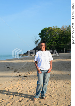 Mature woman standing on tropical beach wearing 90s style normcore fashion jeans and white t-shirt Mature woman standing on tropical beach wearing 90s style normcore fashion jeans and white t-shirt 137028868
