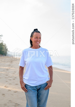 Mature woman standing on tropical beach wearing 90s style normcore fashion jeans and white t-shirt 137028884
