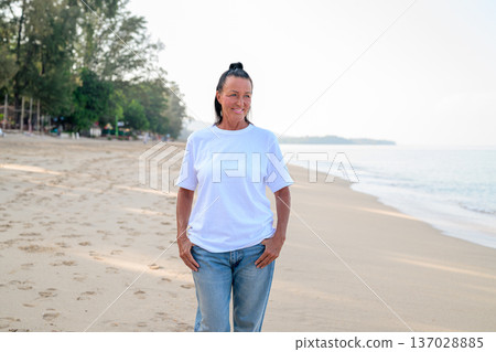 Mature woman standing on tropical beach wearing 90s style normcore fashion jeans and white t-shirt 137028885