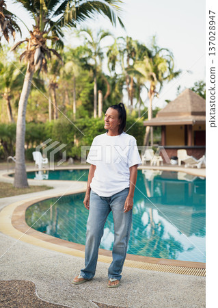 Smiling beautiful older Scandinavian tourist woman standing near swimming pool during holiday 137028947