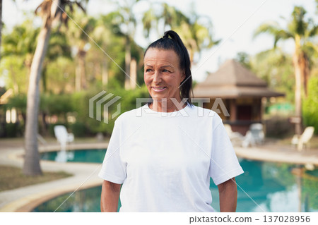 Smiling beautiful older Scandinavian tourist woman standing near swimming pool during holiday 137028956