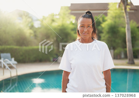 Smiling beautiful older Scandinavian tourist woman standing near swimming pool during holiday Smiling beautiful older Scandinavian tourist woman standing near swimming pool during holiday 137028968