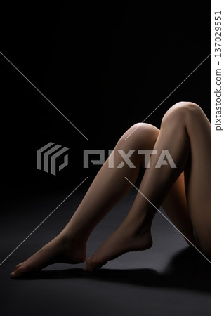 Elegant pose of bare legs under soft lighting in a dark setting Elegant pose of bare legs under soft lighting in a dark setting 137029551