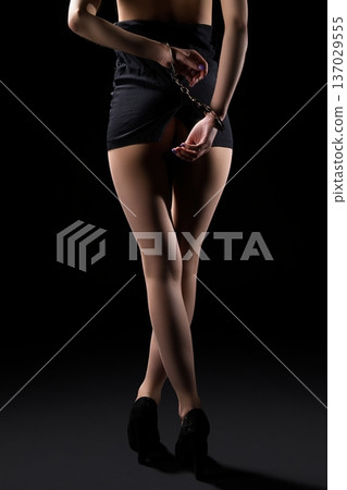 Woman in black skirt poses handcuffed against a dark backdrop Woman in black skirt poses handcuffed against a dark backdrop 137029555