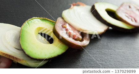 chopped vegetables black tomatoes, avocado and onions against black stone board chopped vegetables black tomatoes, avocado and onions against black stone board 137029899