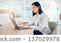一位亞裔女商業領袖在明亮的辦公室裡用筆記型電腦工作。 137029978