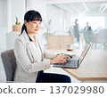 一位女上班族在寬敞的辦公室裡用筆記型電腦打字。 137029980