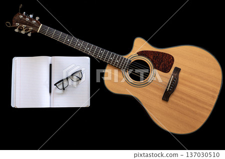 Classical acoustic guitar and an open notebook on a black background. 137030510
