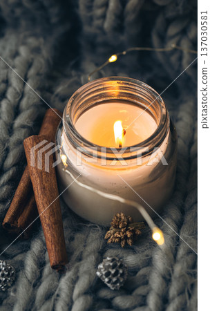 Close-up, candle and cinnamon sticks on the background of a gray knitted element. Close-up, candle and cinnamon sticks on the background of a gray knitted element. 137030581