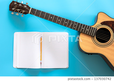 Acoustic guitar and notepad on a blue background, top view. Acoustic guitar and notepad on a blue background, top view. 137030742