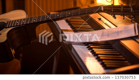 acoustic guitar stands on piano with notes, close-up, beautiful color background acoustic guitar stands on piano with notes, close-up, beautiful color background 137030753