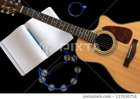 Acoustic guitar, tambourine, notepad and coffee cup on black background. Acoustic guitar, tambourine, notepad and coffee cup on black background. 137030758
