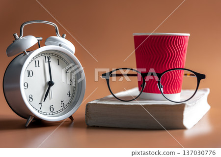Alarm clock, cup of coffee, glasses and book, morning concept. Alarm clock, cup of coffee, glasses and book, morning concept. 137030776