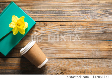 Book, paper disposable cup and yellow narcissus flower on wooden background. 137031142
