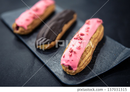 Chocolate and berry eclairs close-up on a black background. Chocolate and berry eclairs close-up on a black background. 137031315