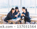 一個高中女生在教室裡一邊看著她的智能手機一邊和她的同學聊天 137031564