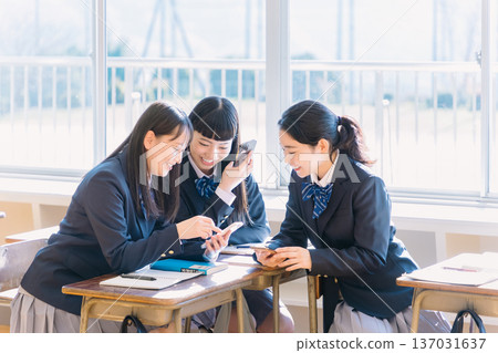 A high school girl talking to her classmate while looking at her smartphone in the classroom 137031637