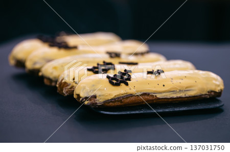 Close-up of eclairs in yellow glaze on a black background. 137031750