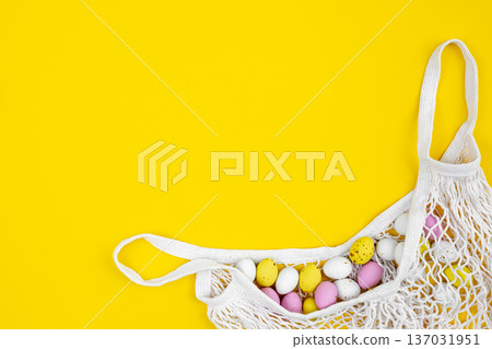 Colored Easter eggs in a mesh bag on a yellow background, flat lay. 137031951