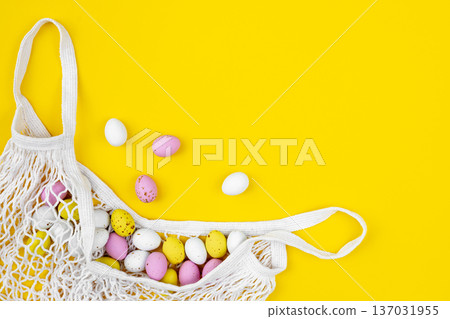Colored Easter eggs in a mesh bag on a yellow background, flat lay. 137031955