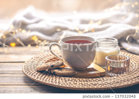 Composition with cup of tea, candles and a knitted element. 137032048