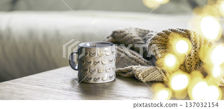 Cozy background with shiny gray cup, bokeh lights and knitted element. Cozy background with shiny gray cup, bokeh lights and knitted element. 137032154