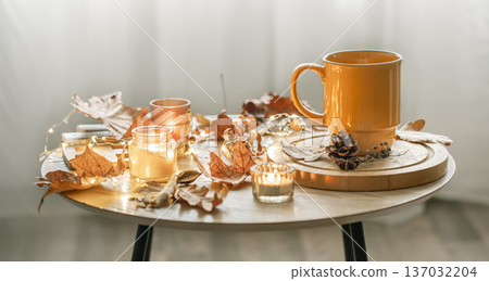 Cozy composition with a cup, candles and autumn leaves in the interior. 137032204