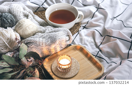 Cozy composition with a cup of tea, a candle and knitted elements on a blanket. Cozy composition with a cup of tea, a candle and knitted elements on a blanket. 137032214